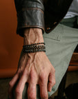 A close-up of a man’s wrist wearing the Ethan Wrap in 18K Gold as a bracelet, styled with a leather jacket for a bold, elevated look.