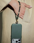 Phone case with a Emerald beaded strap held by a person wearing a beige coat.
