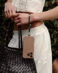 Close-up of the Leah Phone Charm in Emerald attached to a phone, styled on model wearing neutral tones.