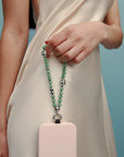 Full view of the Jade Leah Phone Charm paired with a blush phone case, held by a model in a cream outfit.