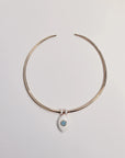 Gold collar necklace featuring a single blue ceramic evil eye charm with white enamel dividers, displayed against a neutral background.