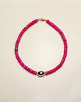 Stella necklace featuring vibrant pink beads with a central evil eye-shaped charm in gold, designed to add a playful and protective touch to any outfit.