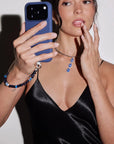 Model holding a phone with the Sapphire Leah Phone Charm while wearing the Mayra Evil Eye Choker Trio, showcasing the full Winter Collection look.