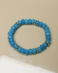 Single Zoe bracelet in azure blue laid flat, featuring smooth beads and gold accents for an elegant look.