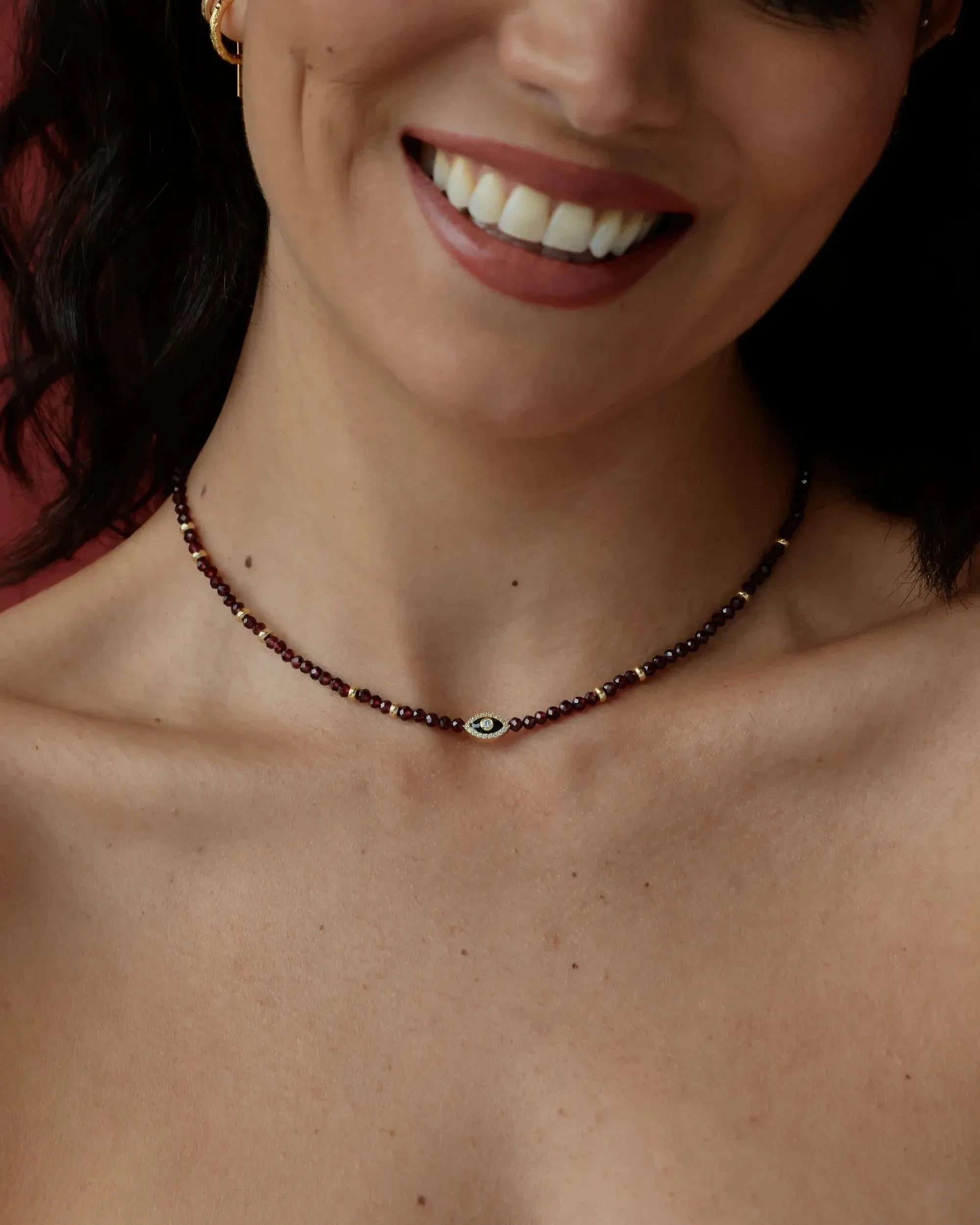 Close-up of a woman wearing a beaded necklace with a visible evil eye symbol.