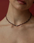 Necklace with a small evil eye charm worn by a person against a red background