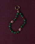 Green beaded charm with gold and purple accents on a dark purple background