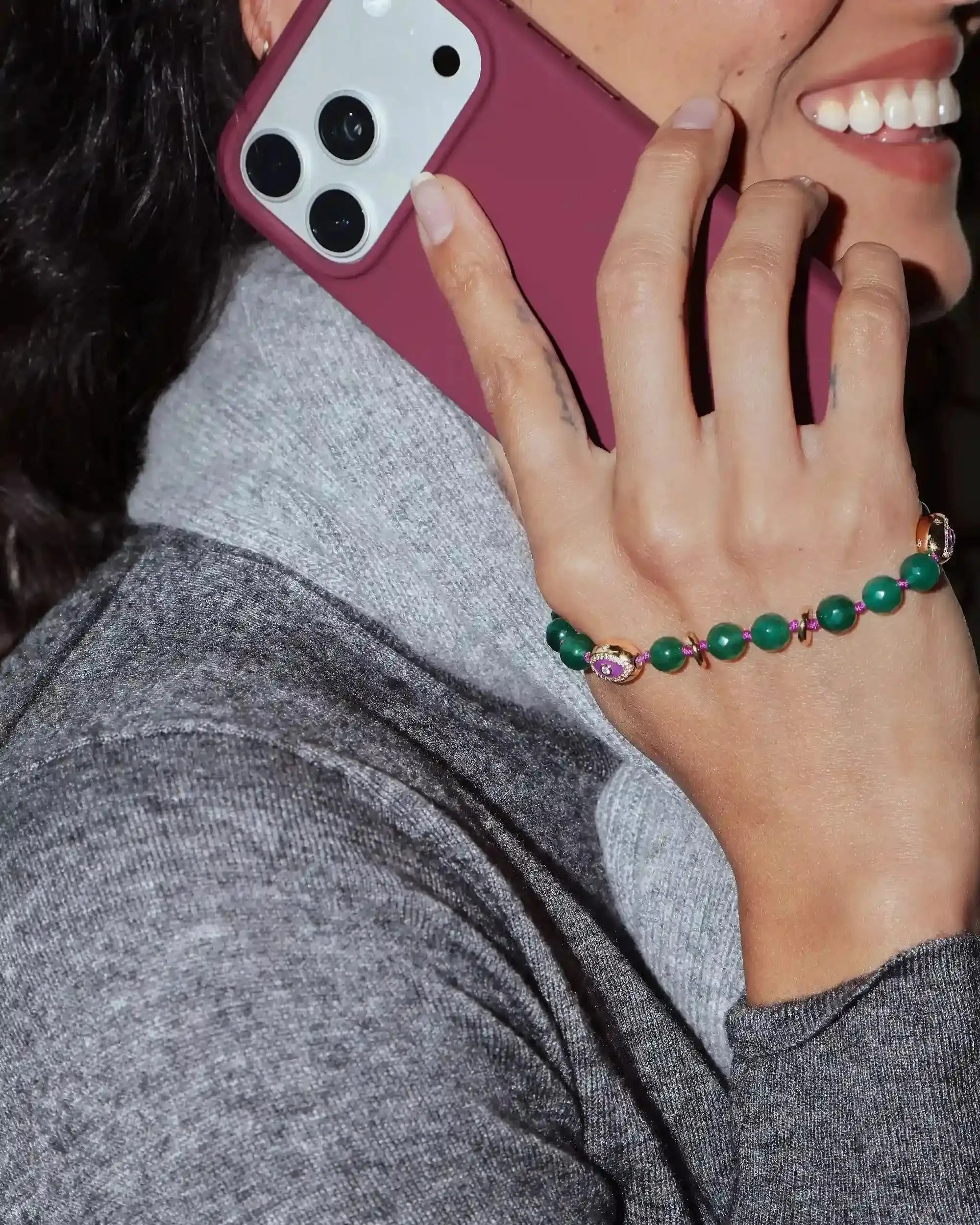 Person holding a phone with a pink case, wearing a green beaded bracelet.