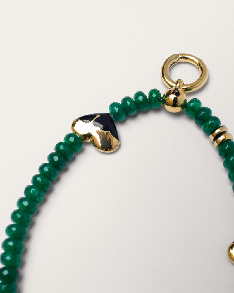 Close-up of the Aria wristlet in emerald quartz, featuring rich green beads and gold-plated heart-shaped charms with black detailing, complete with a gold ring attachment.