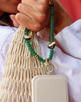 Close-up of a hand holding both a net bag and white mobile phone by its beaded strap