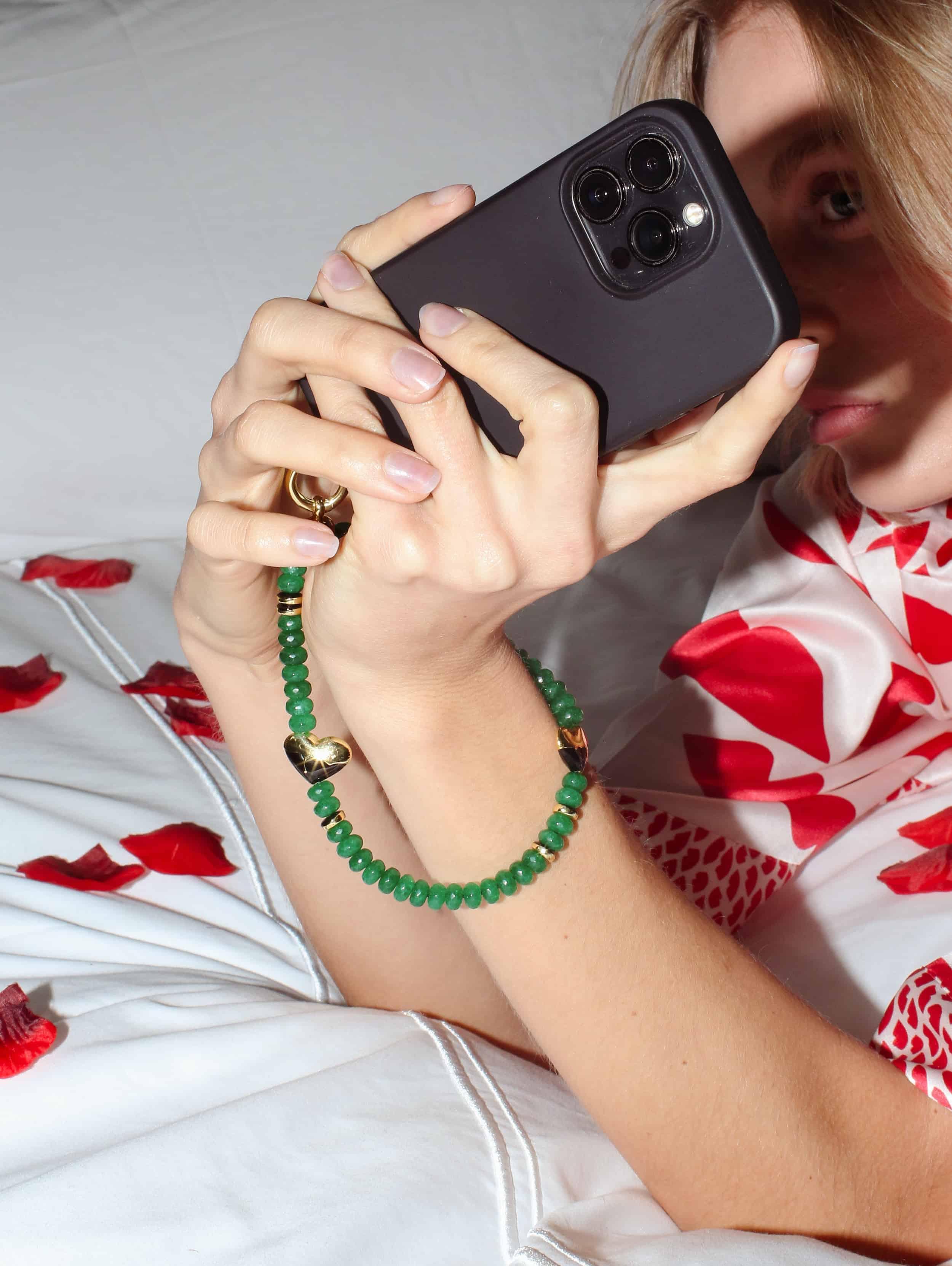 an emerald green wristlet phone strap around the wrist of a woman taking a selfie