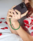 an emerald green wristlet phone strap around the wrist of a woman taking a selfie