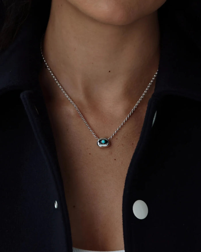 Necklace with a turquoise gemstone evil eye pendant worn by a person against a dark background