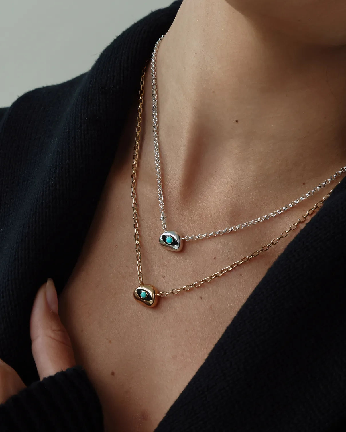 Necklace with a small evil eye pendant with a turquoise gemstone on a model wearing a black top.