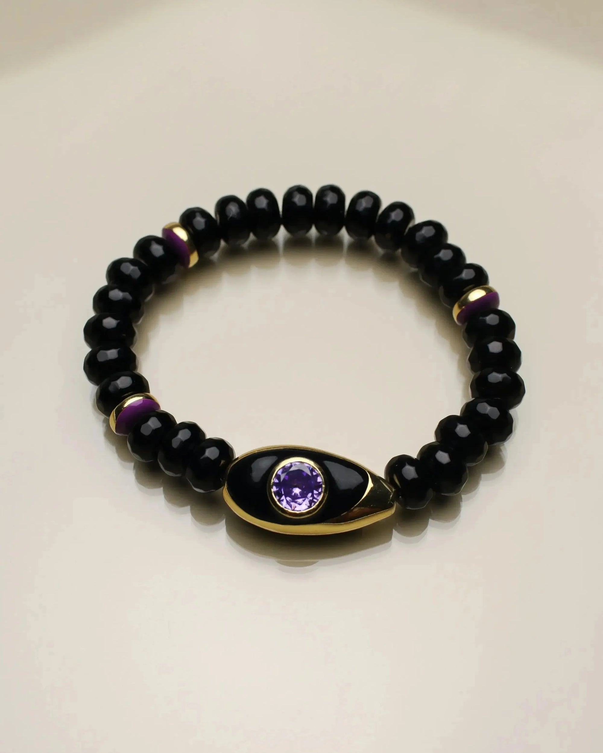 Aya bracelet with onyx quartz beads, accented with purple and gold dividers, featuring an evil eye charm with a purple CZ stone.&quot;