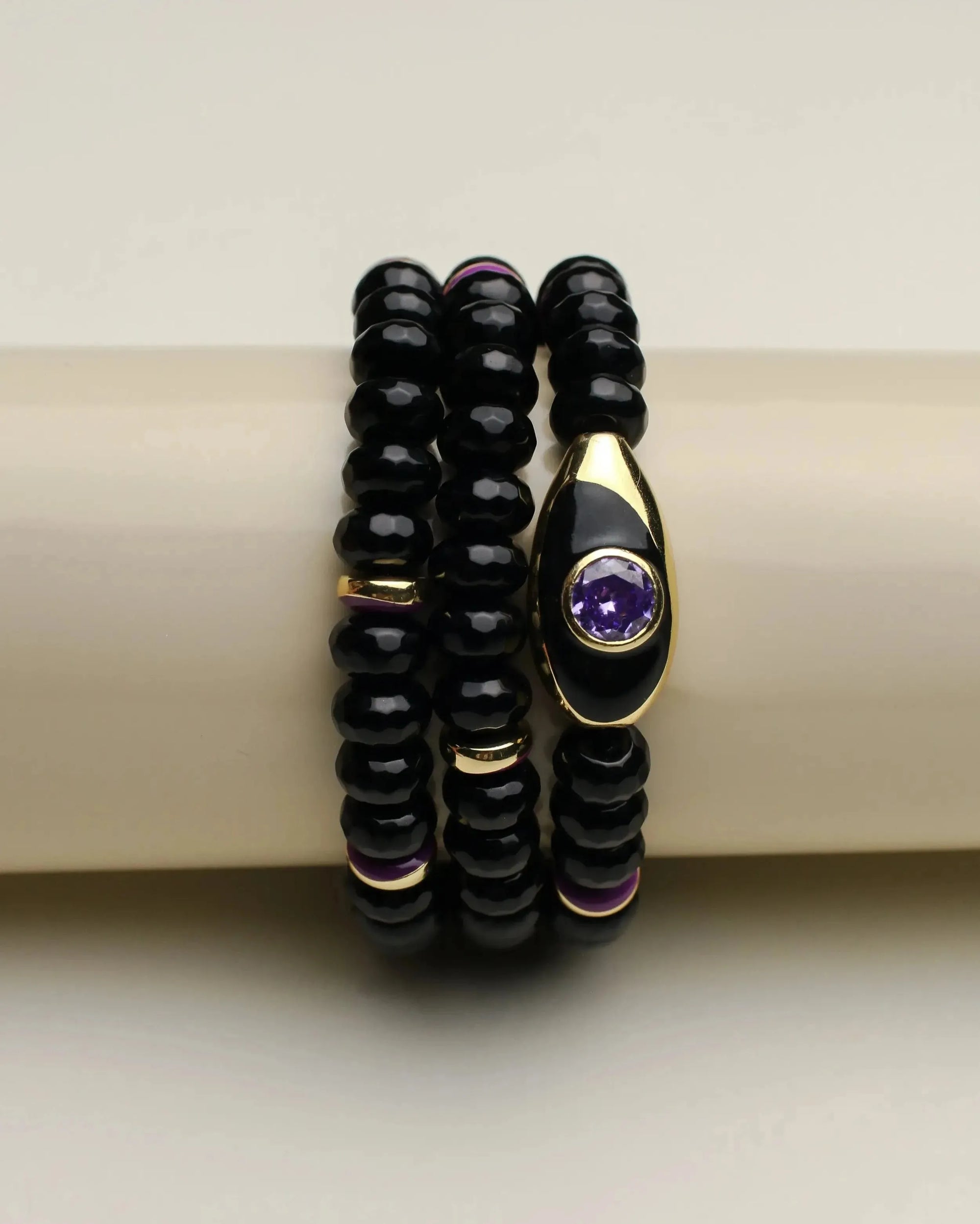 Stack of three Aya onyx quartz  bracelets with gold accents and purple details, displayed elegantly on a bracelet holder.