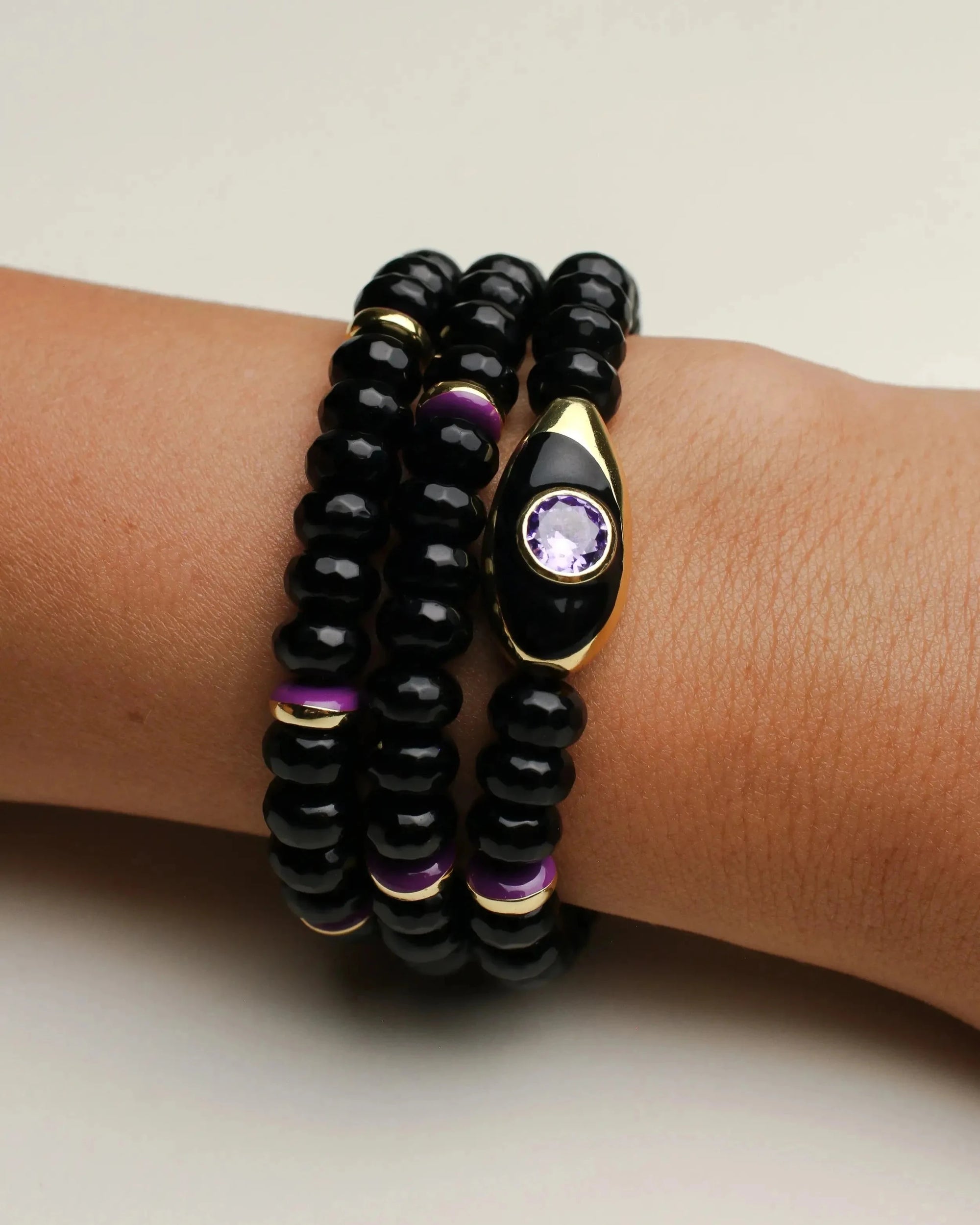 Aya onyx quartz bracelet stack worn on the wrist, highlighting the evil eye charm with a purple CZ stone and gold-plated accents for a luxe, layered style.