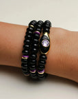 Aya onyx quartz bracelet stack worn on the wrist, highlighting the evil eye charm with a purple CZ stone and gold-plated accents for a luxe, layered style.