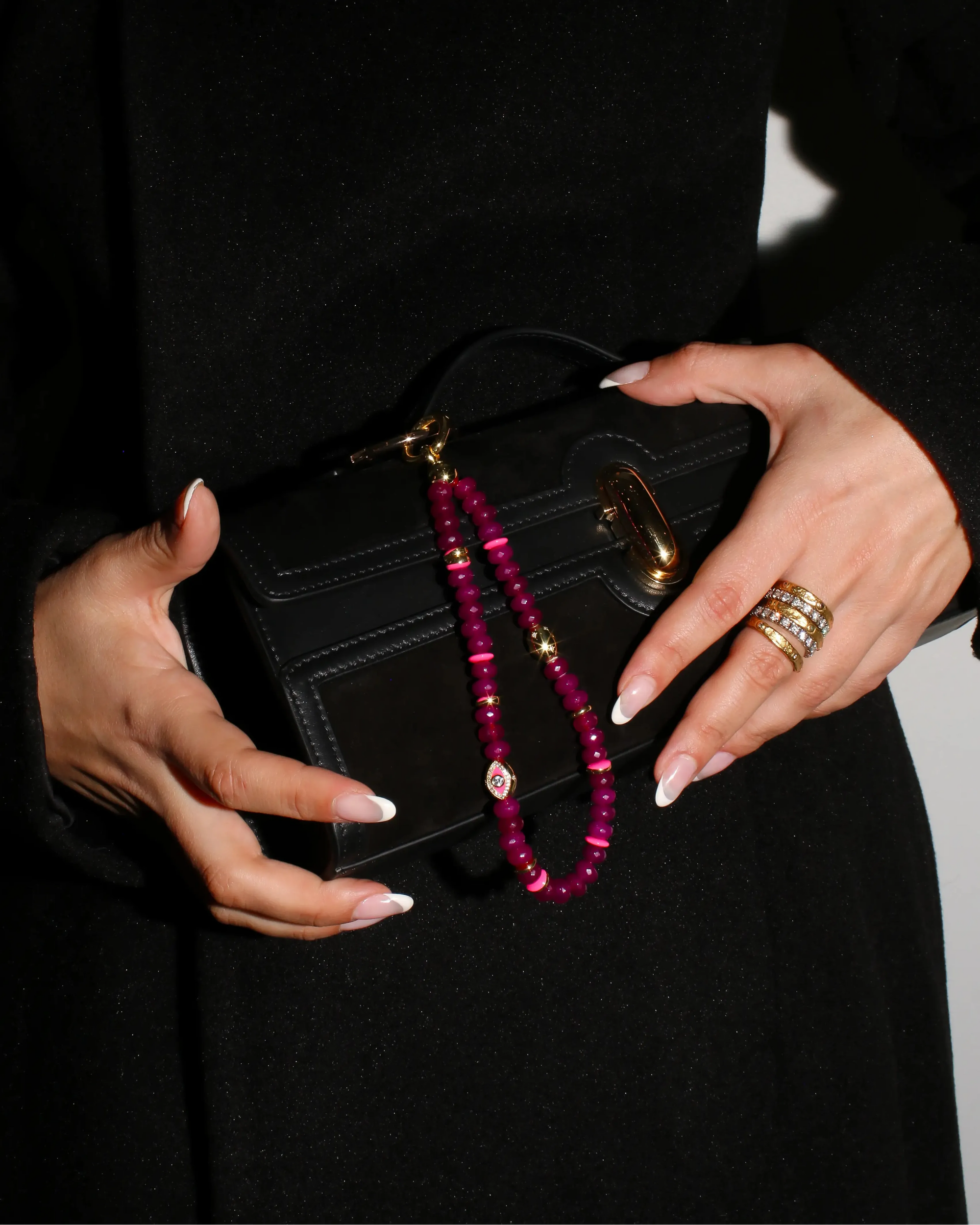 Leah Bag Charm held with a black clutch – A hand elegantly holding the amethyst quartz charm attached to a black clutch, showcasing its refined and sophisticated appeal.