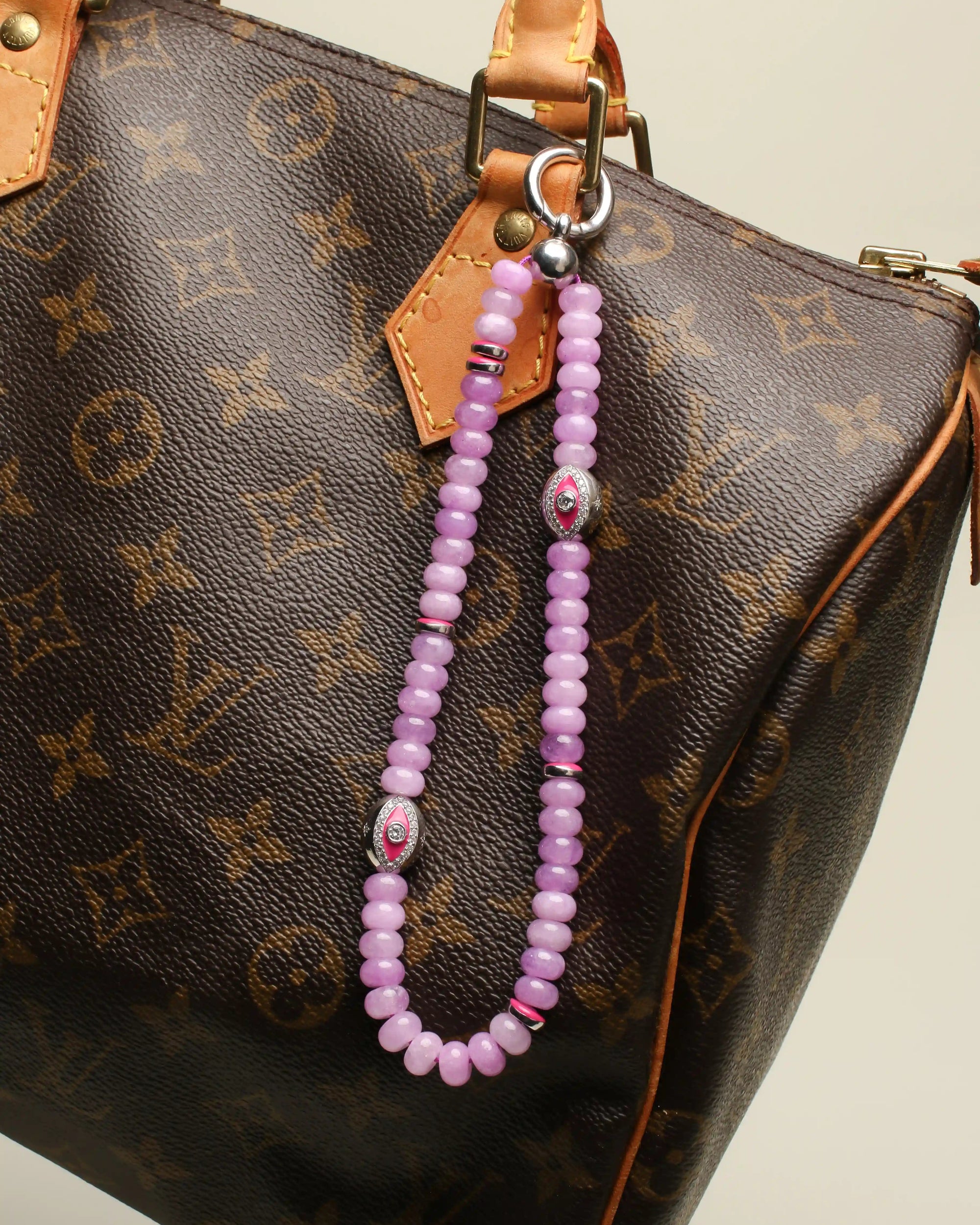 Leah Bag Charm attached to a luxury brown monogram handbag – The lavender quartz charm clipped onto a brown leather designer bag, demonstrating its versatility and stylish appeal.