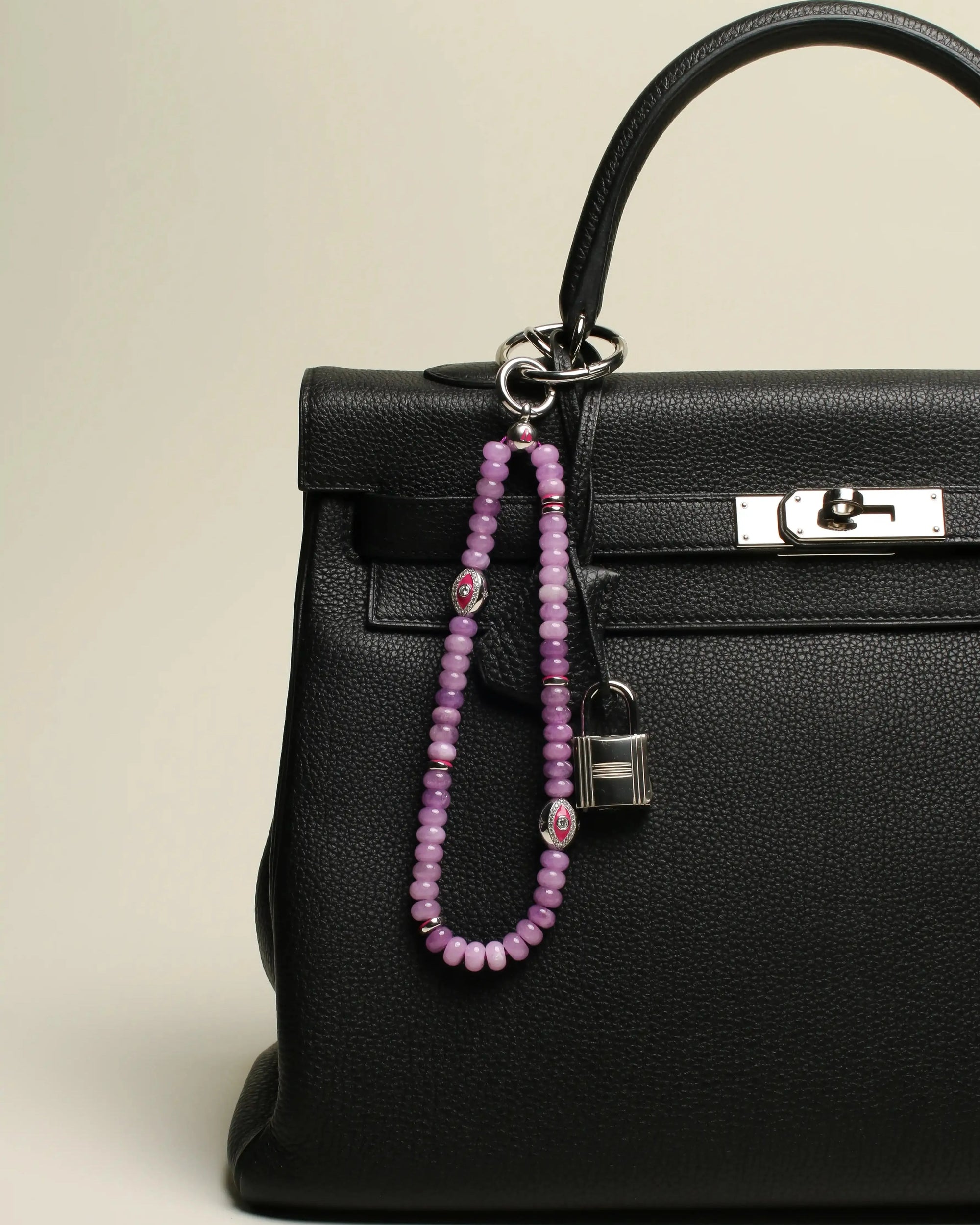 Leah Bag Charm attached to a black handbag – The lavender quartz charm clipped onto a black designer handbag, showcasing its elegant and energy-infused accent.