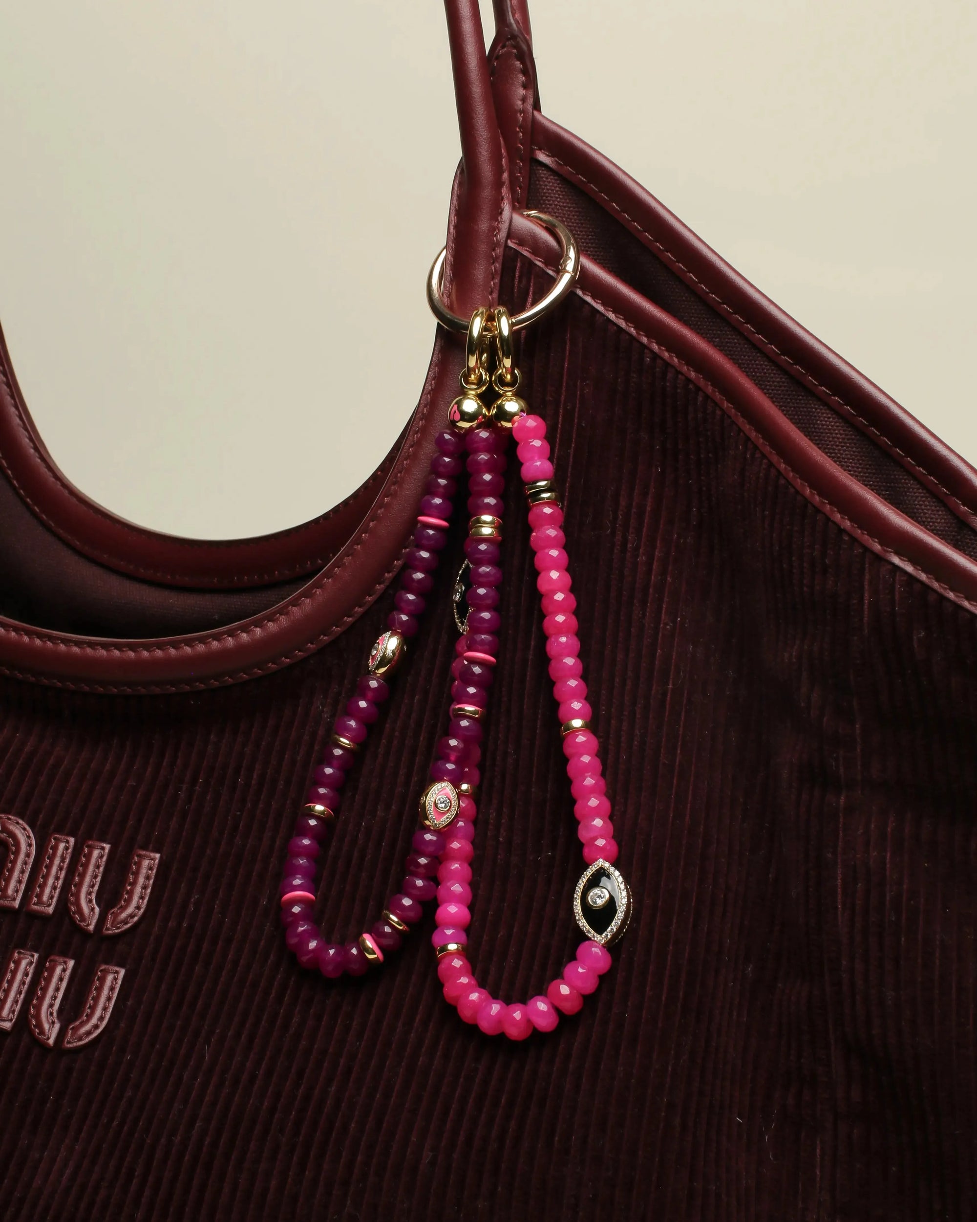 Leah Bag Charm in Amethyst &amp; Stella Bag Charm in Pink attached to a burgundy designer tote – A stylish display of two bag charms, one in faceted amethyst quartz and the other in vibrant pink quartz, clipped onto a burgundy leather designer bag, showcasing their bold yet elegant accents.