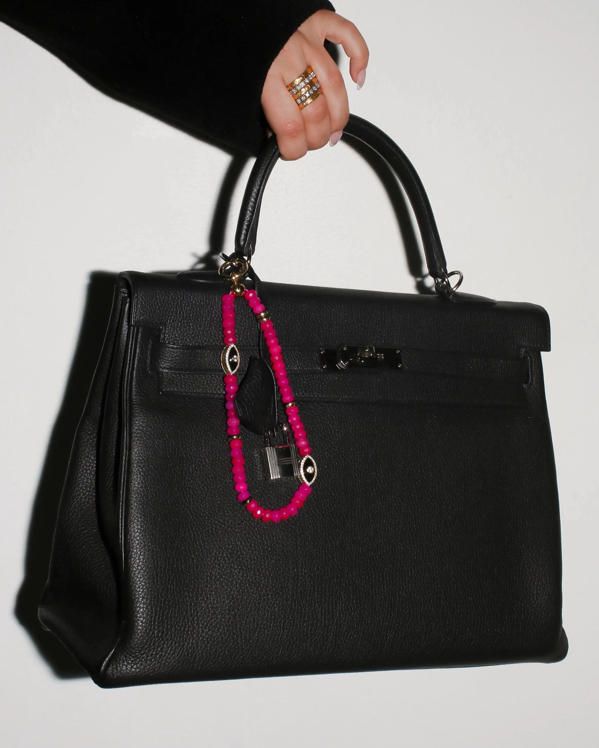 Stella Bag Charm attached to a black handbag – The pink quartz charm clipped onto a structured black handbag, adding a statement of confidence and sophistication.