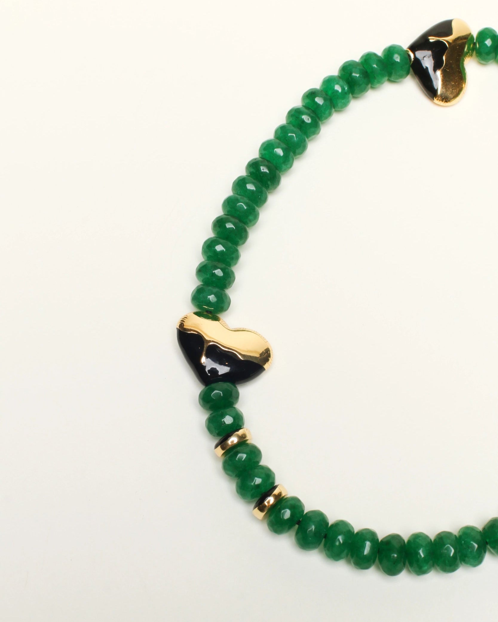 A close-up of The Aria Bag Charm in Emerald, emphasizing the intricate details of the gold-plated heart charm, polished dividers, and faceted emerald quartz beads.