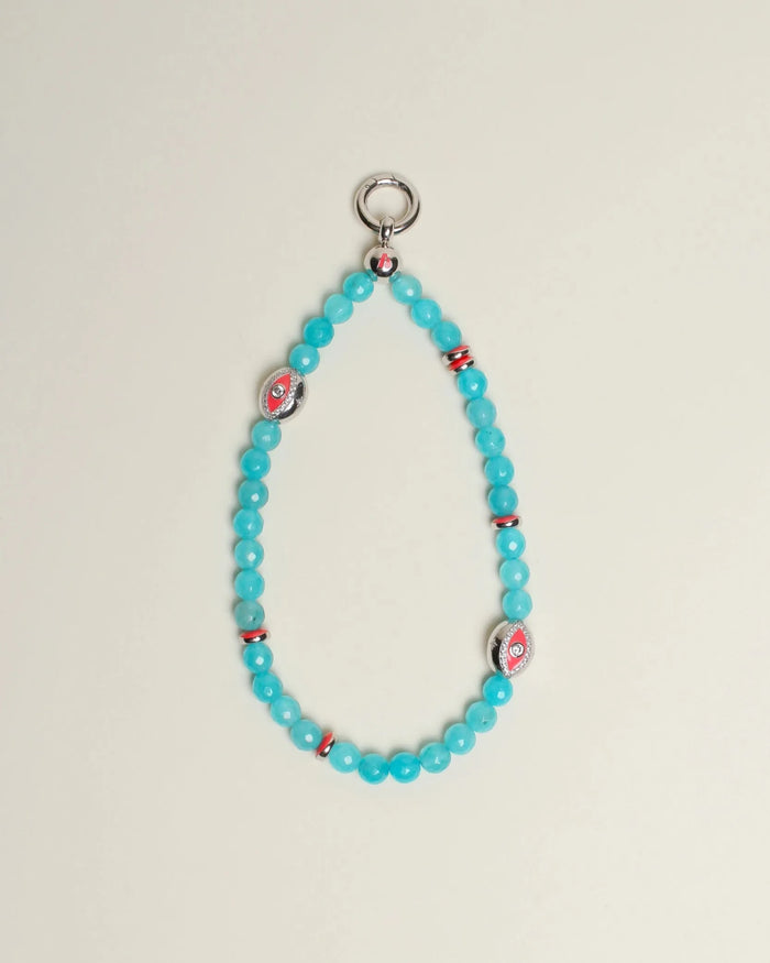 The Leah Bag Charm in Turquoise displayed against a neutral background, showcasing its faceted turquoise quartz beads, rhodium-plated silver Evil Eye charms, and pink accent dividers.