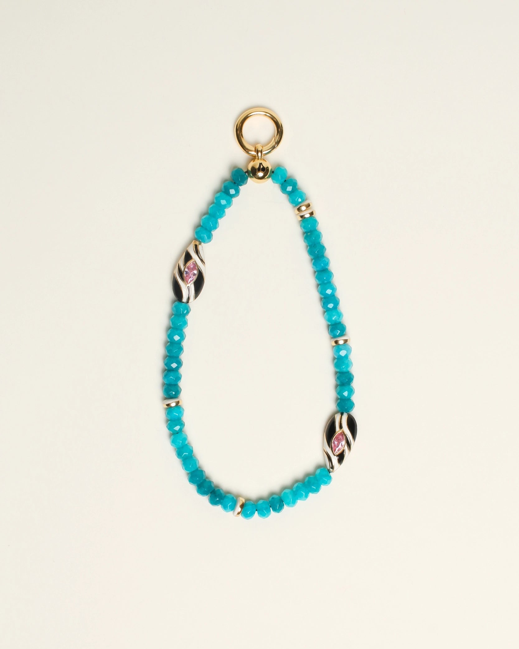 The Minou Bag Charm in Turquoise displayed against a neutral background, showcasing its semi-precious turquoise quartz beads, 14k gold-plated accents, and zebra-striped Evil Eye charms for a striking and meaningful design.