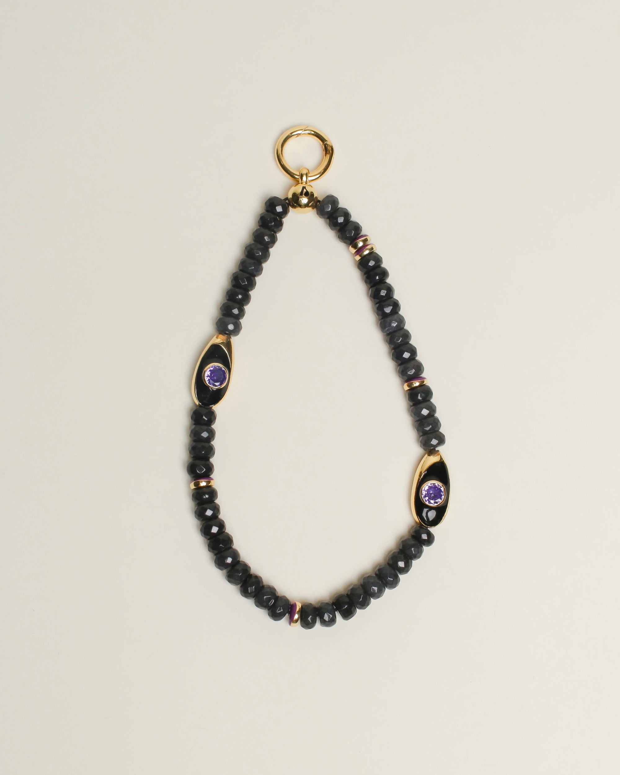 The Aya Bag Charm in Onyx displayed against a neutral background, showcasing its semi-precious onyx beads, 14k gold-plated accents, and amethyst-adorned Evil Eye charms for a powerful and elegant design.