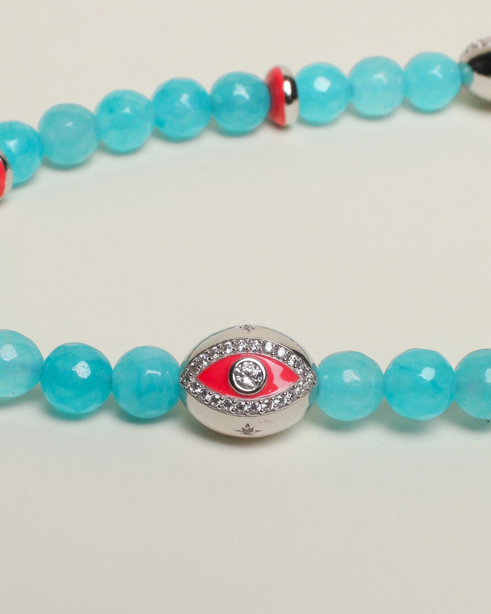 A close-up of The Leah Bag Charm in Turquoise, highlighting the intricate details of the rhodium-plated silver Evil Eye charm, pink dividers, and semi-precious turquoise quartz beads.