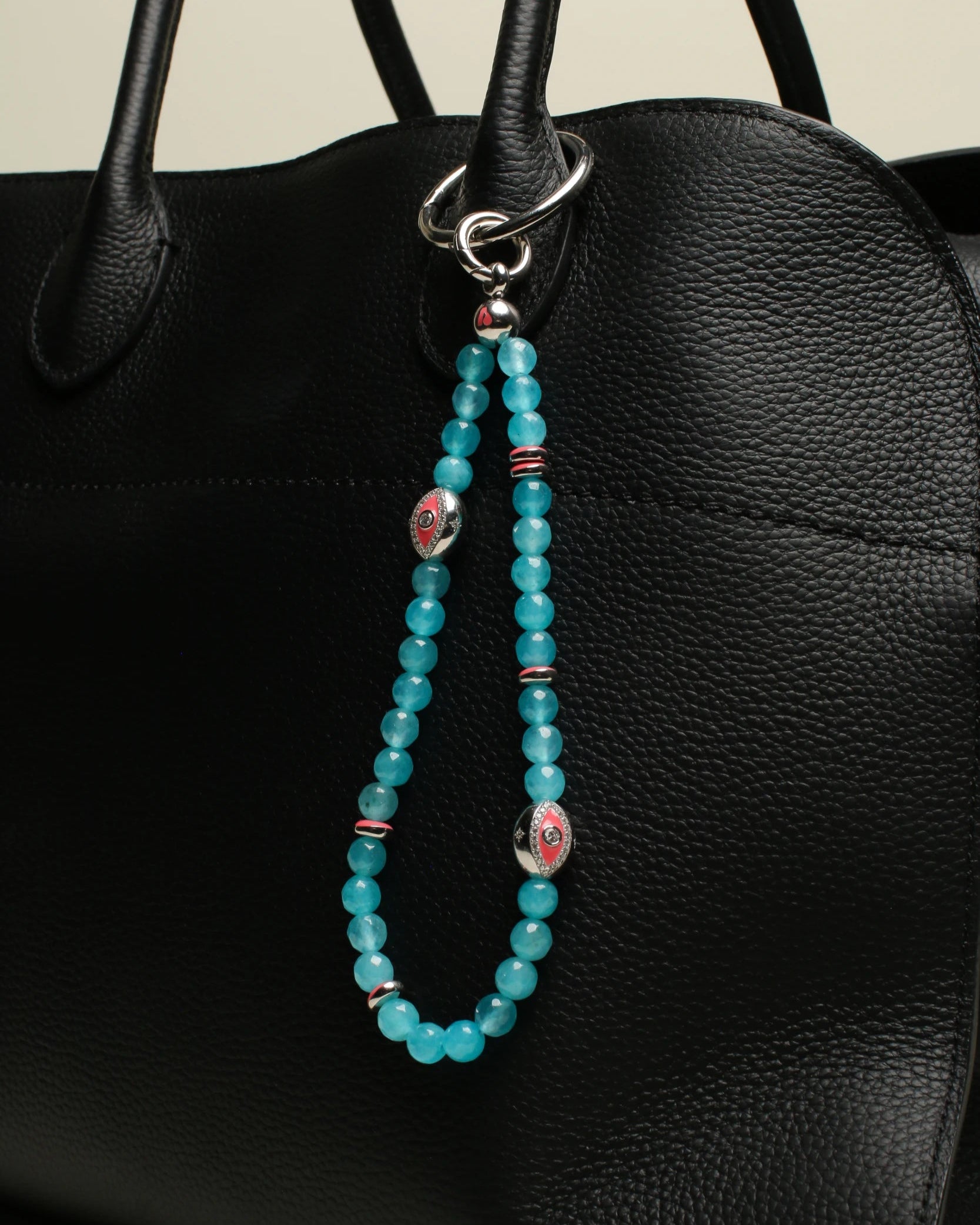 A black handbag adorned with The Leah Bag Charm in Turquoise, emphasizing its bright turquoise quartz beads and silver Evil Eye charms for a striking contrast.