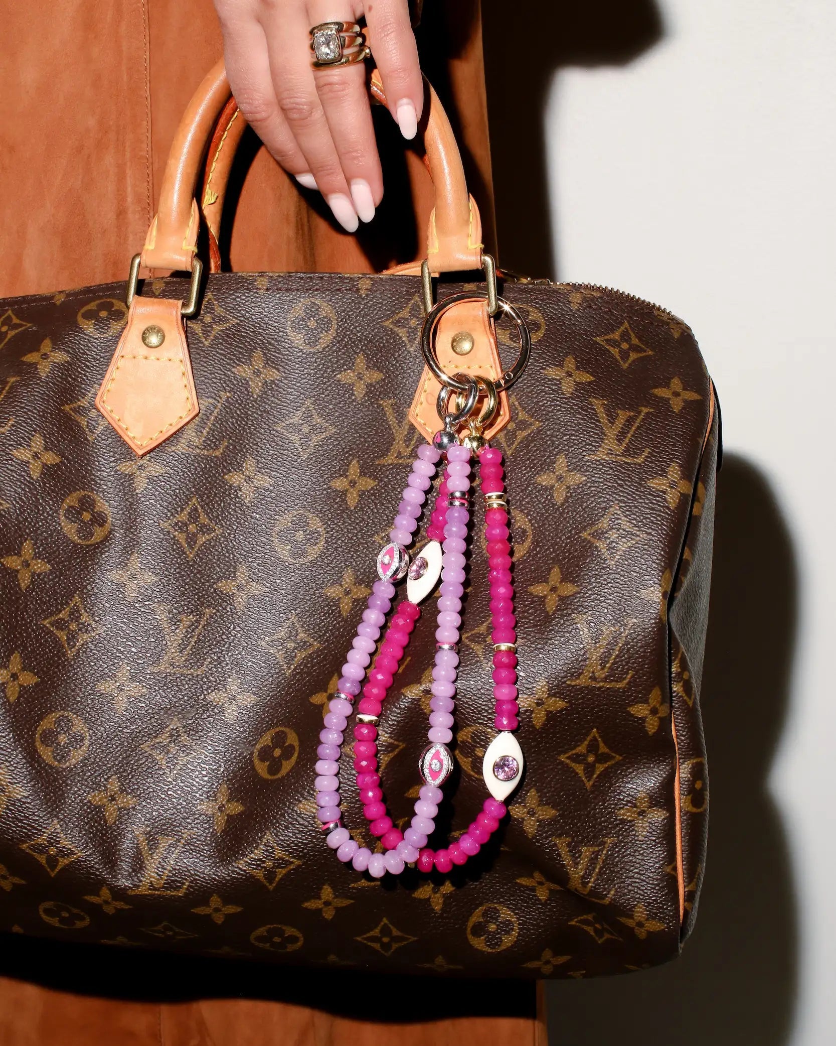 A model carries a designer handbag adorned with The Mano Bag Charm in Pink, showcasing its rich pink quartz beads and eye-shaped charms for a statement of elegance and protection.