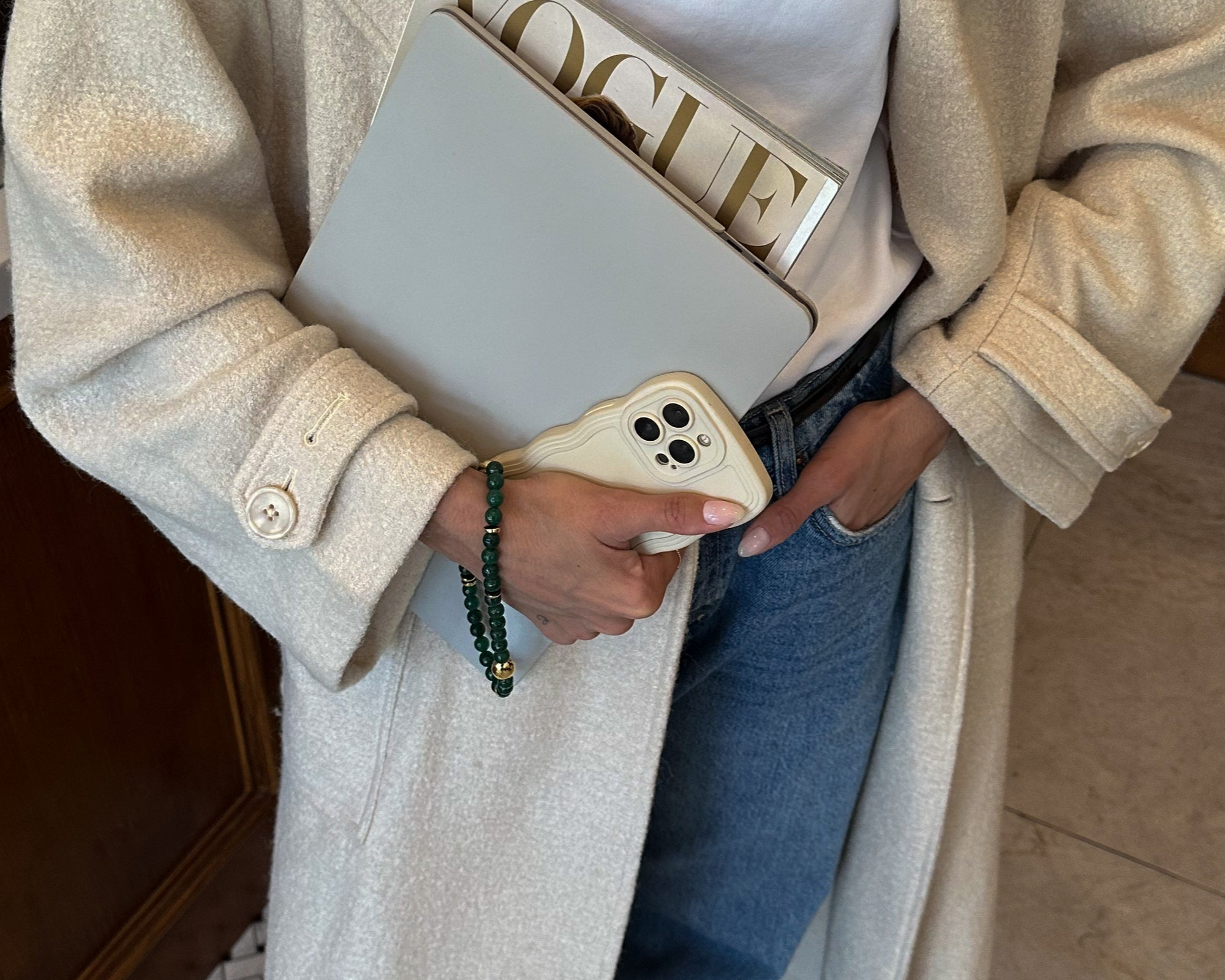 Person holding a phone and a magazine, wearing a beige coat and blue jeans.