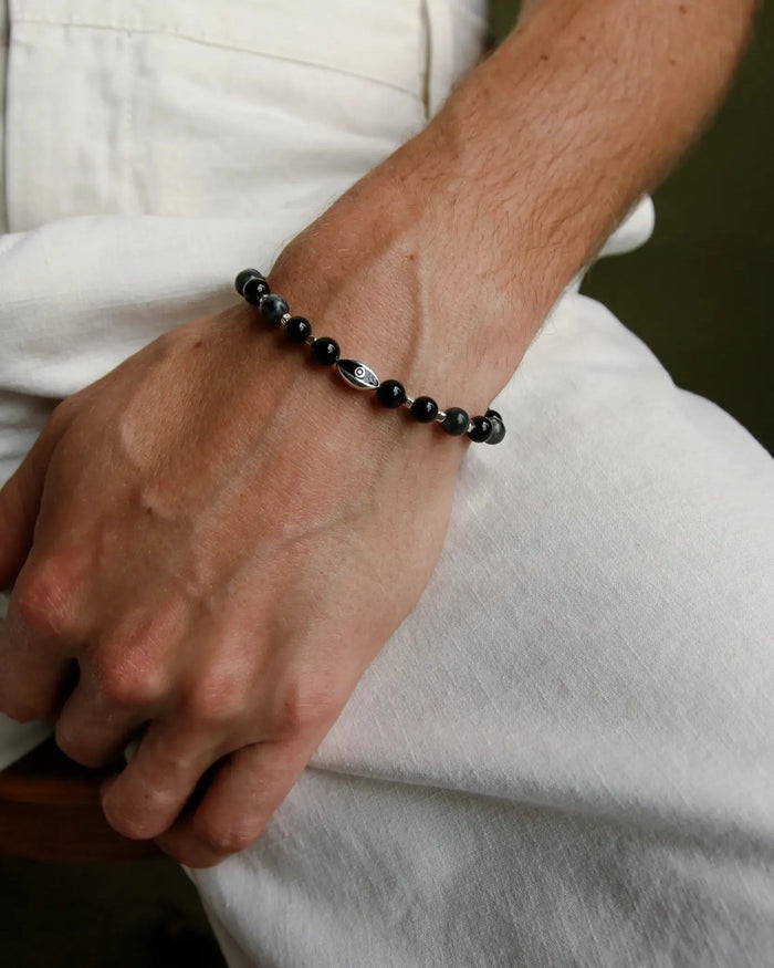 A man wearing the David Bracelet in Silver, featuring 6mm Onyx and Black Labradorite Quartz beads with a black CZ diamond evil eye charm.