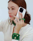 Model holding a phone with one hand, wearing the Leah Mini Wristlet in emerald as a phone accessory. The matching Leah bracelet set on the wrist and Lilou Necklace adds a layered, stylish touch to the look.