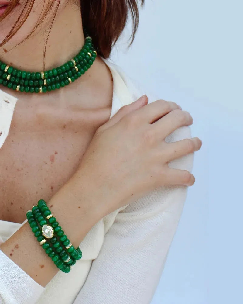 Woman wearing the lilou emerald beaded necklace and matching leah emerald bracelet stack with gold accents, styled with a light cream cardigan. The jewelry showcases vibrant green quartz beads, emphasizing elegance and balance.