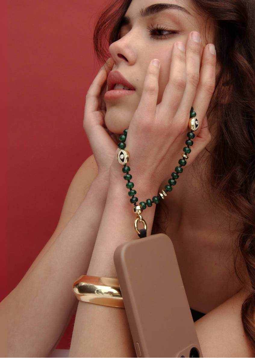 Woman wearing a green beaded necklace and gold bracelet against a red background