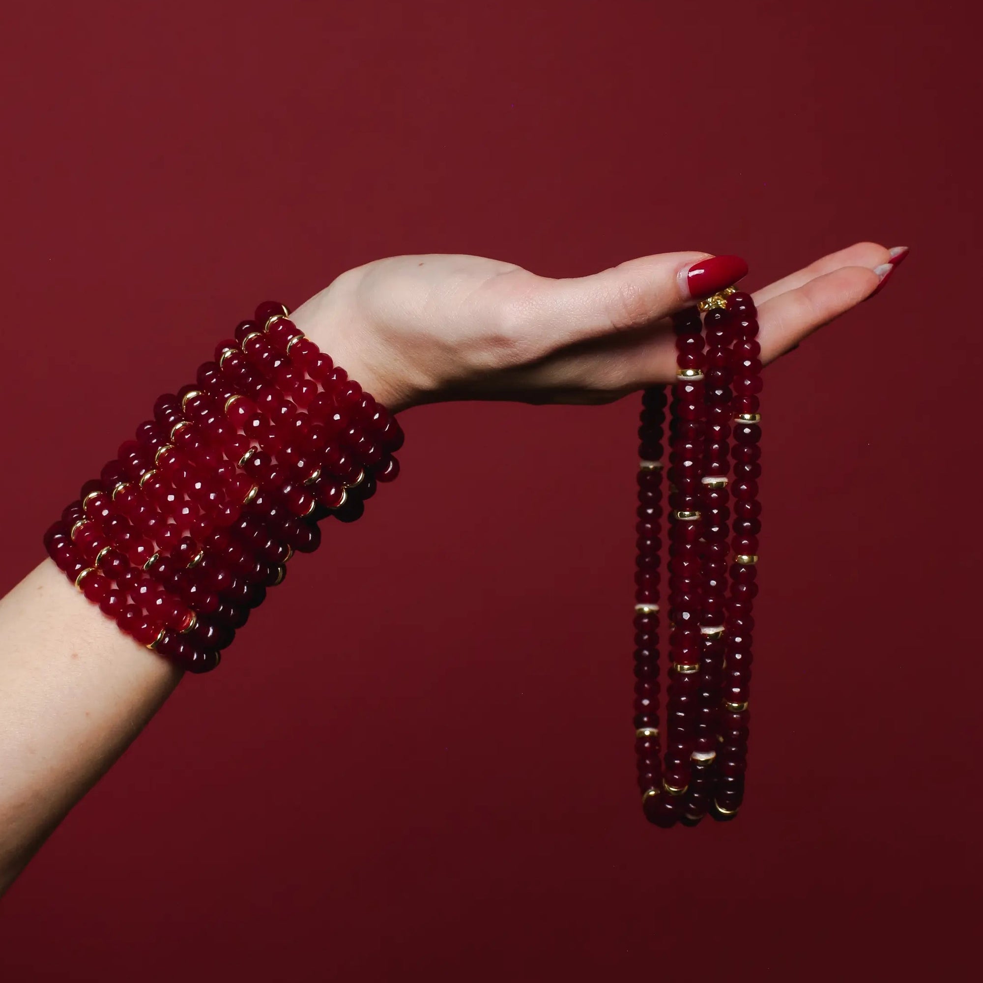 Hand wearing a red beaded bracelet against a red background