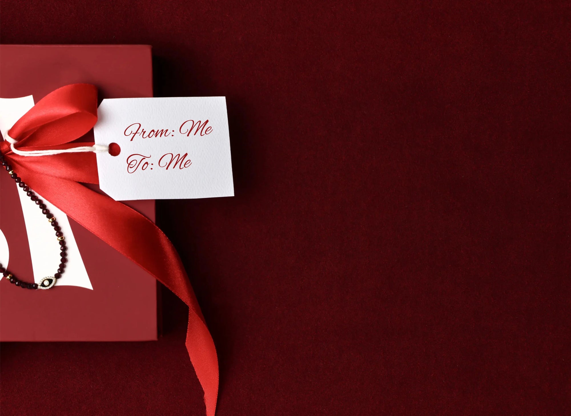 Red gift box with a red ribbon with Juliana gemstone bead necklace and 'From: Me To: Me' tag on a dark red background