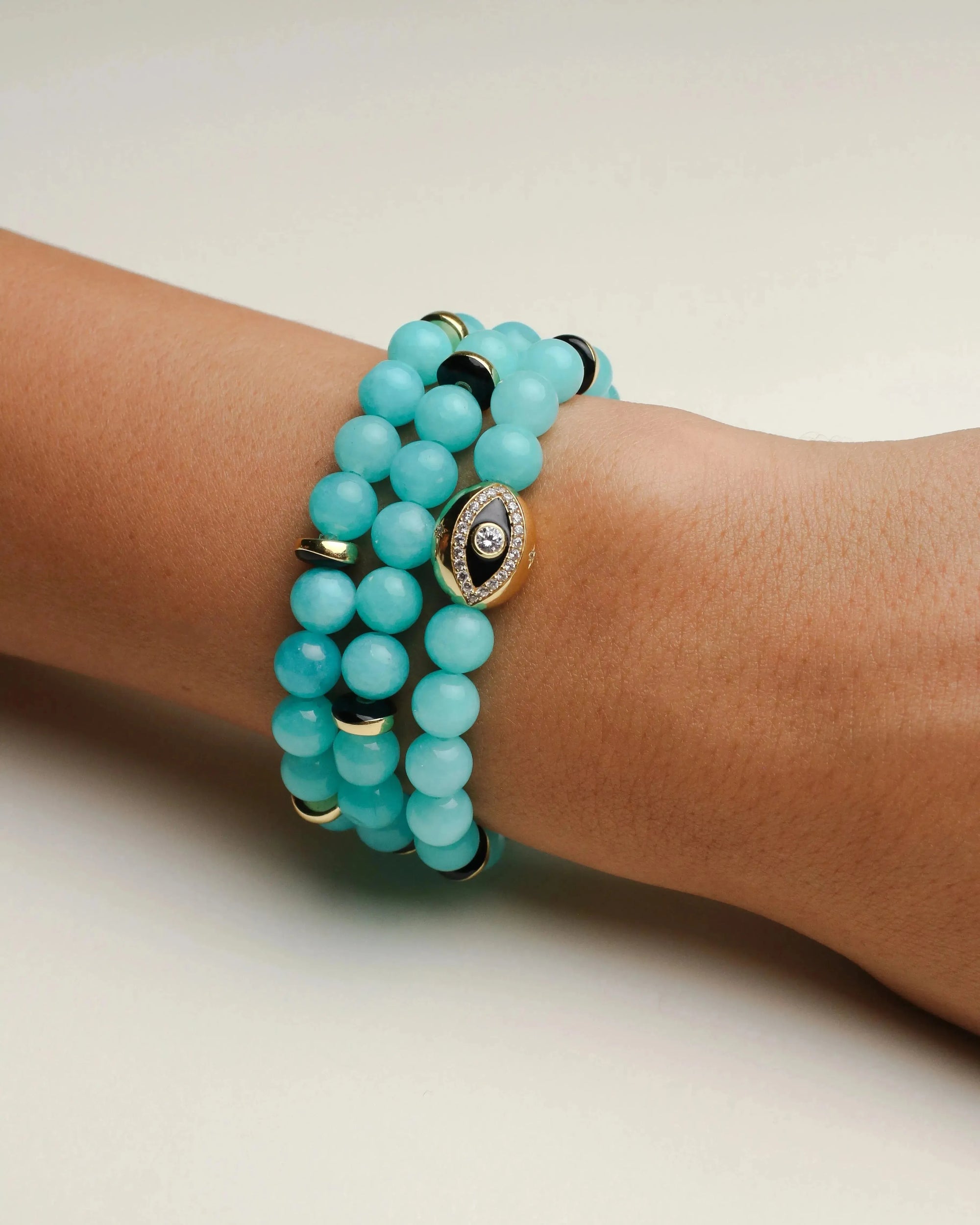 A set of three Leah aqua bracelets worn on the wrist, featuring soft blue beads with gold accents and a central eye charm for a chic and vibrant stack.