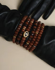 Stacked Leah bracelet set in caramel displayed over sleek black leather gloves, showcasing faceted beads, gold accents, and the iconic evil eye charm.