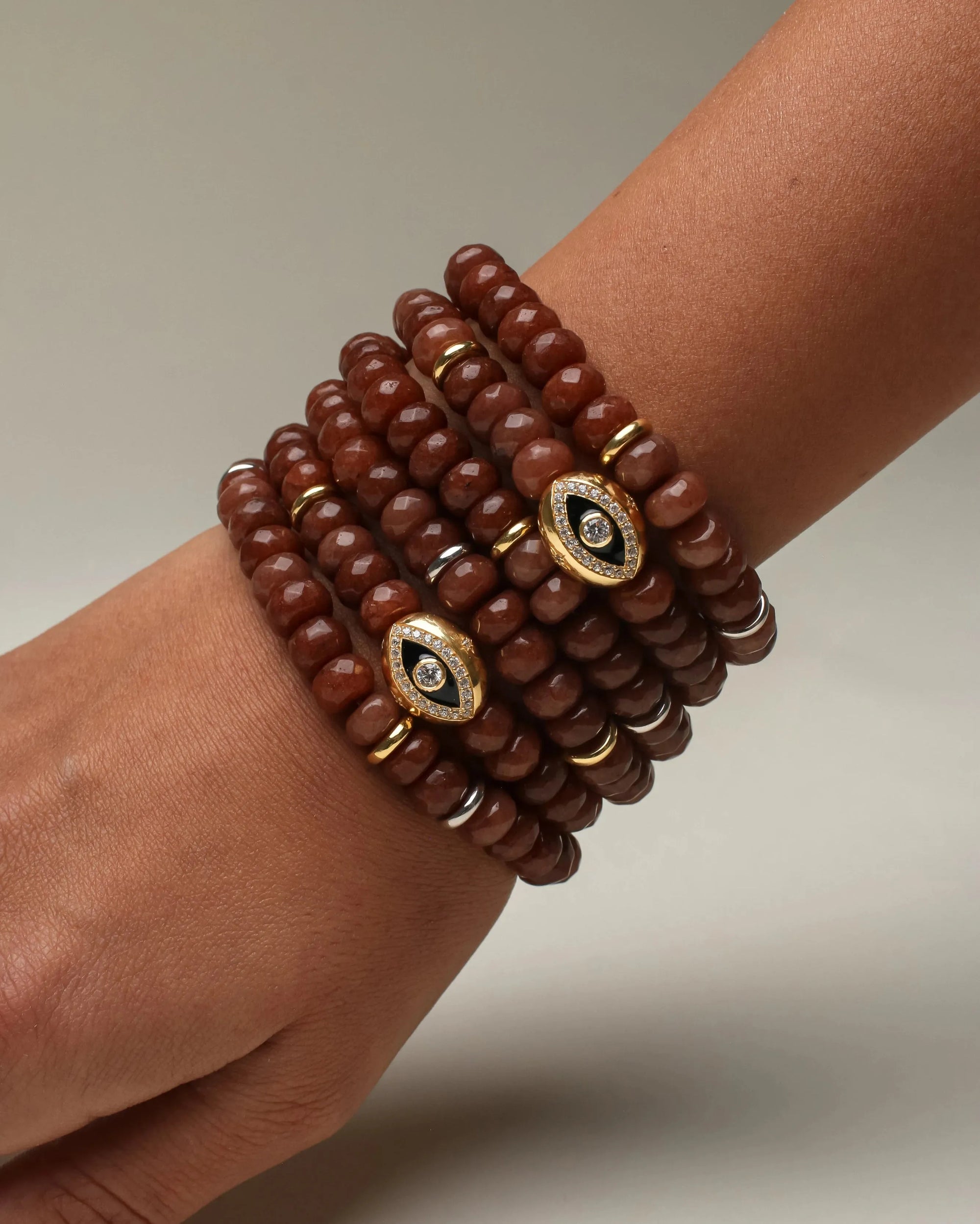 Close-up of the Leah bracelet stack in caramel, elegantly wrapped around a wrist, featuring rich faceted beads with gold accents and a gold evil eye charm adorned with crystals.