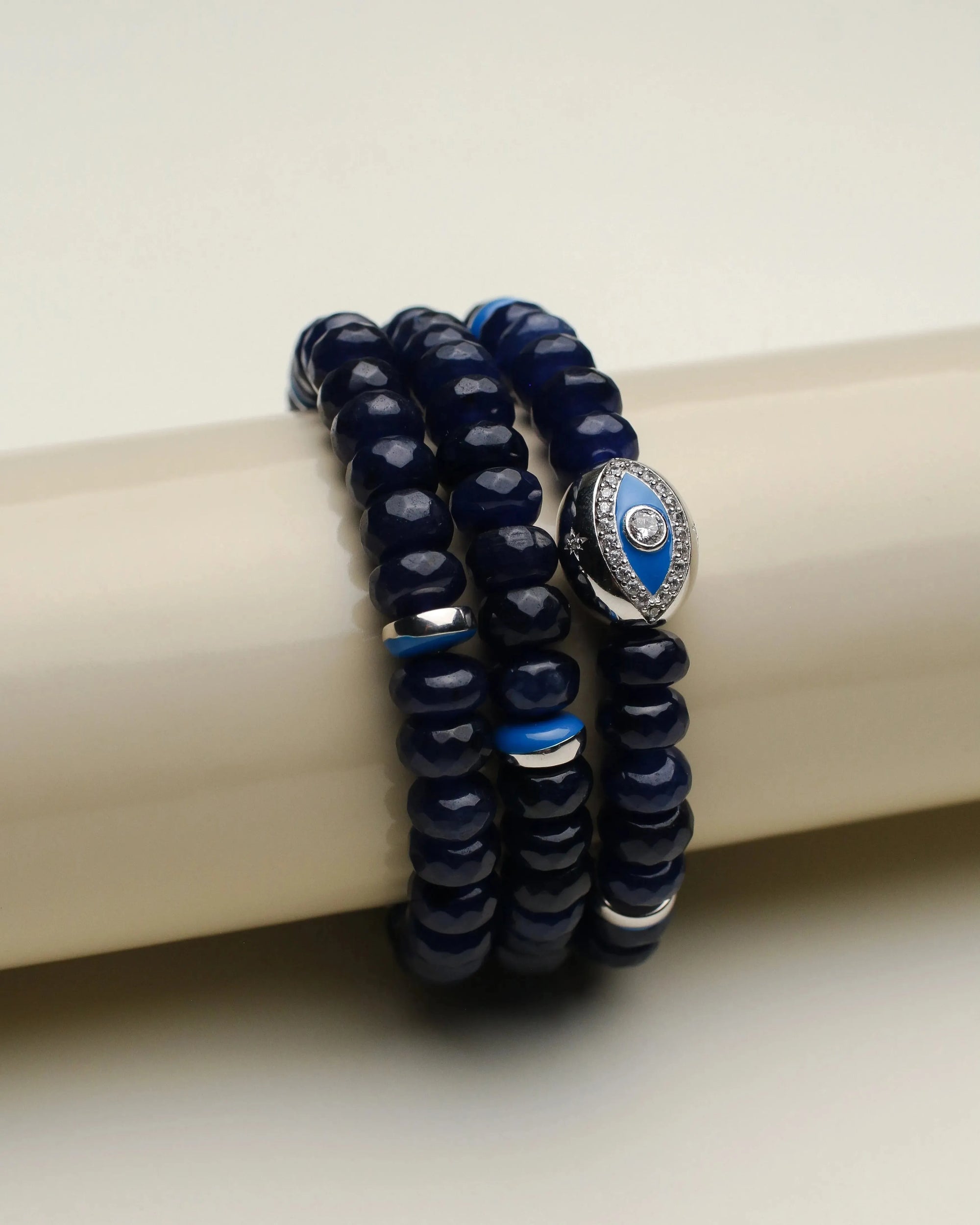 Leah sapphire quartz bracelets displayed on a cylindrical stand, highlighting the rich blue beads with silver accents and the eye-catching evil eye charm.