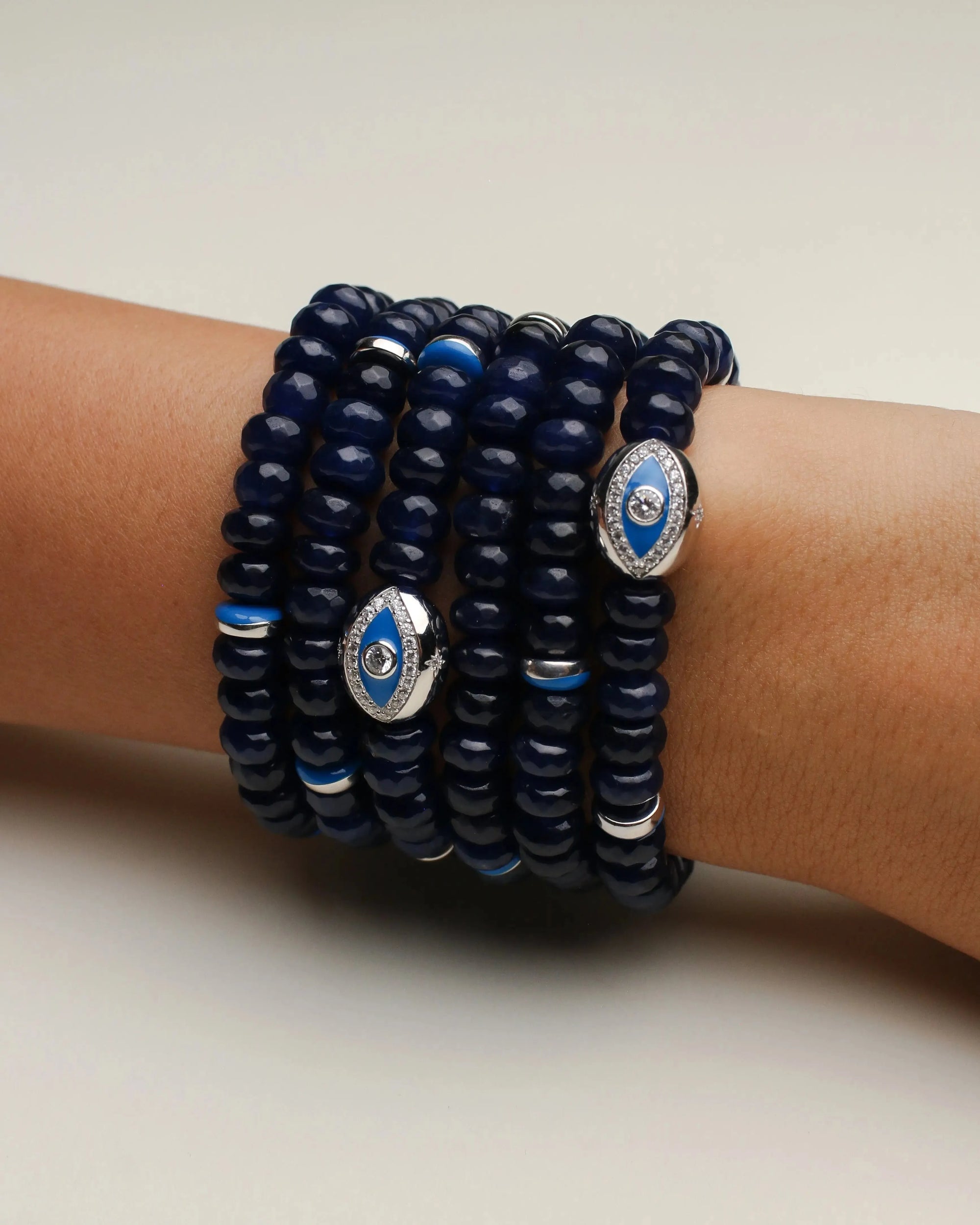 Leah sapphire quartz bracelet six stacked on a wrist, showcasing the dark blue beads, silver detailing, and an elegant evil eye charm at the center.