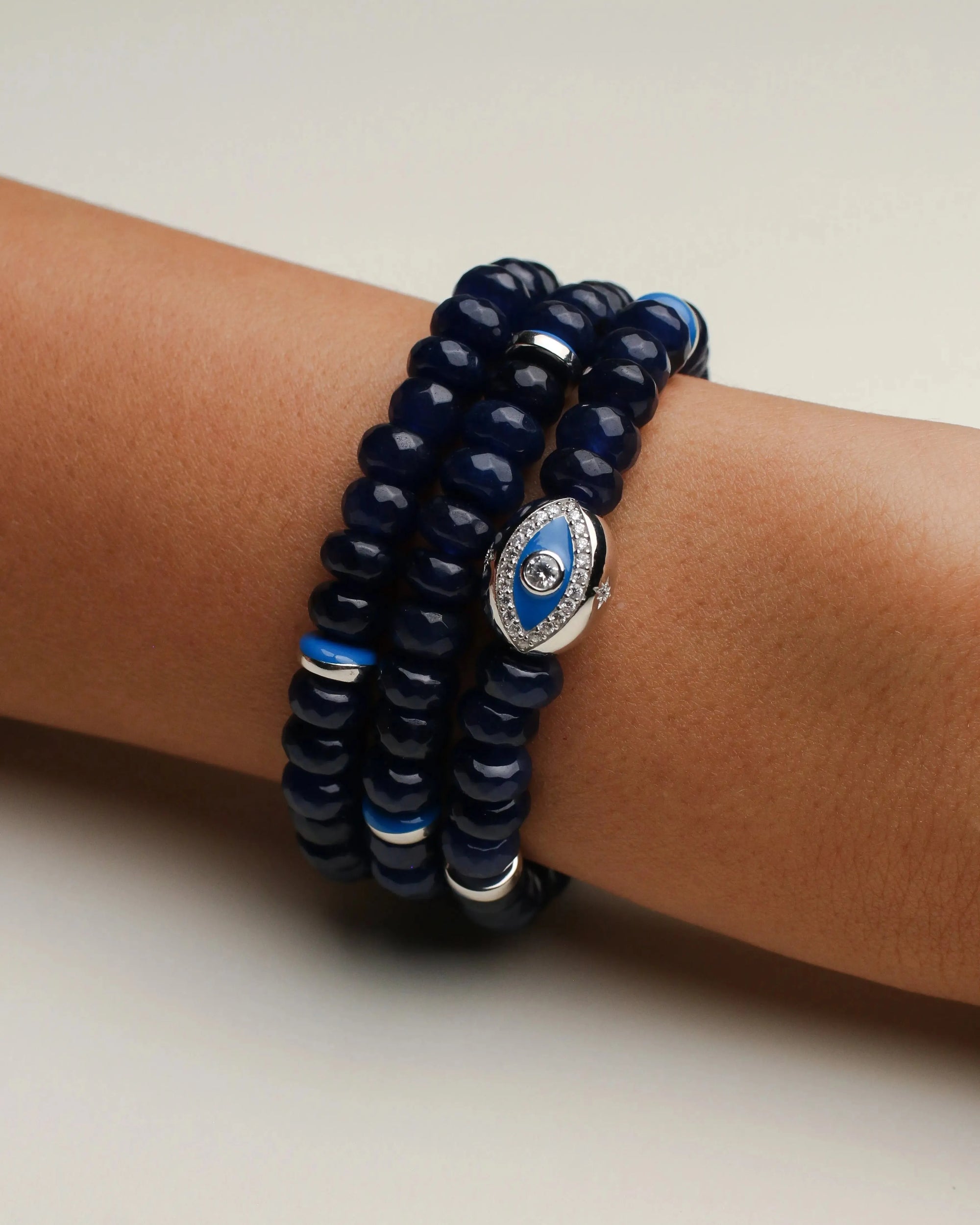 A set of three Leah sapphire quartz bracelets worn on the wrist, featuring deep blue beads with silver accents and a prominent evil eye charm for a striking layered look.