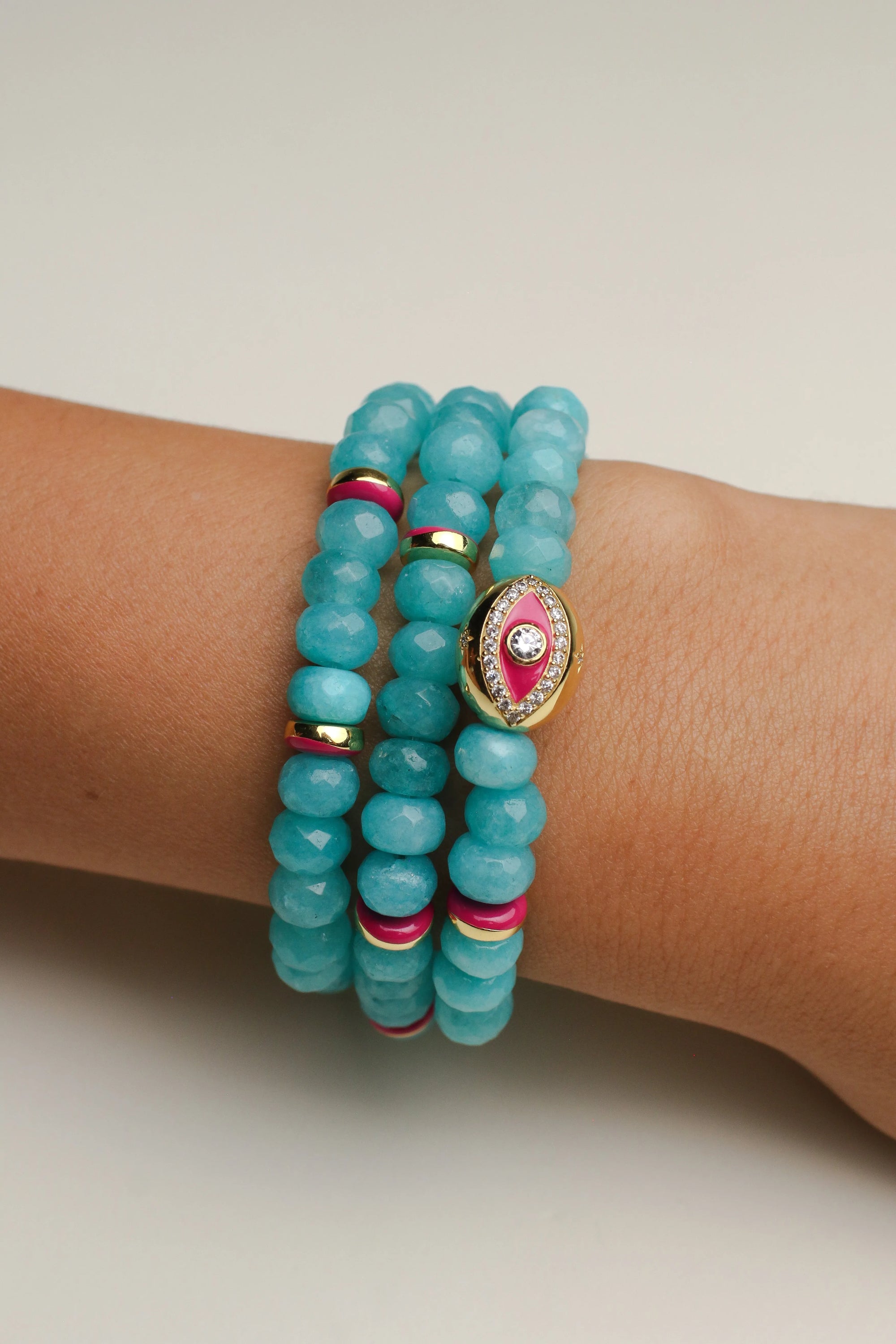 A set of three Leah turquoise bracelets worn on the wrist, featuring vibrant blue-green beads with pink and gold accents and a central eye charm for a playful and bold look.