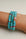 A set of three Leah turquoise bracelets worn on the wrist, featuring vibrant blue-green beads with pink and gold accents and a central eye charm for a playful and bold look.