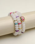 Leah white bracelet set of three displayed on a cylindrical stand, showcasing the smooth white beads with vibrant pink, blue, and gold accents and a central eye charm.